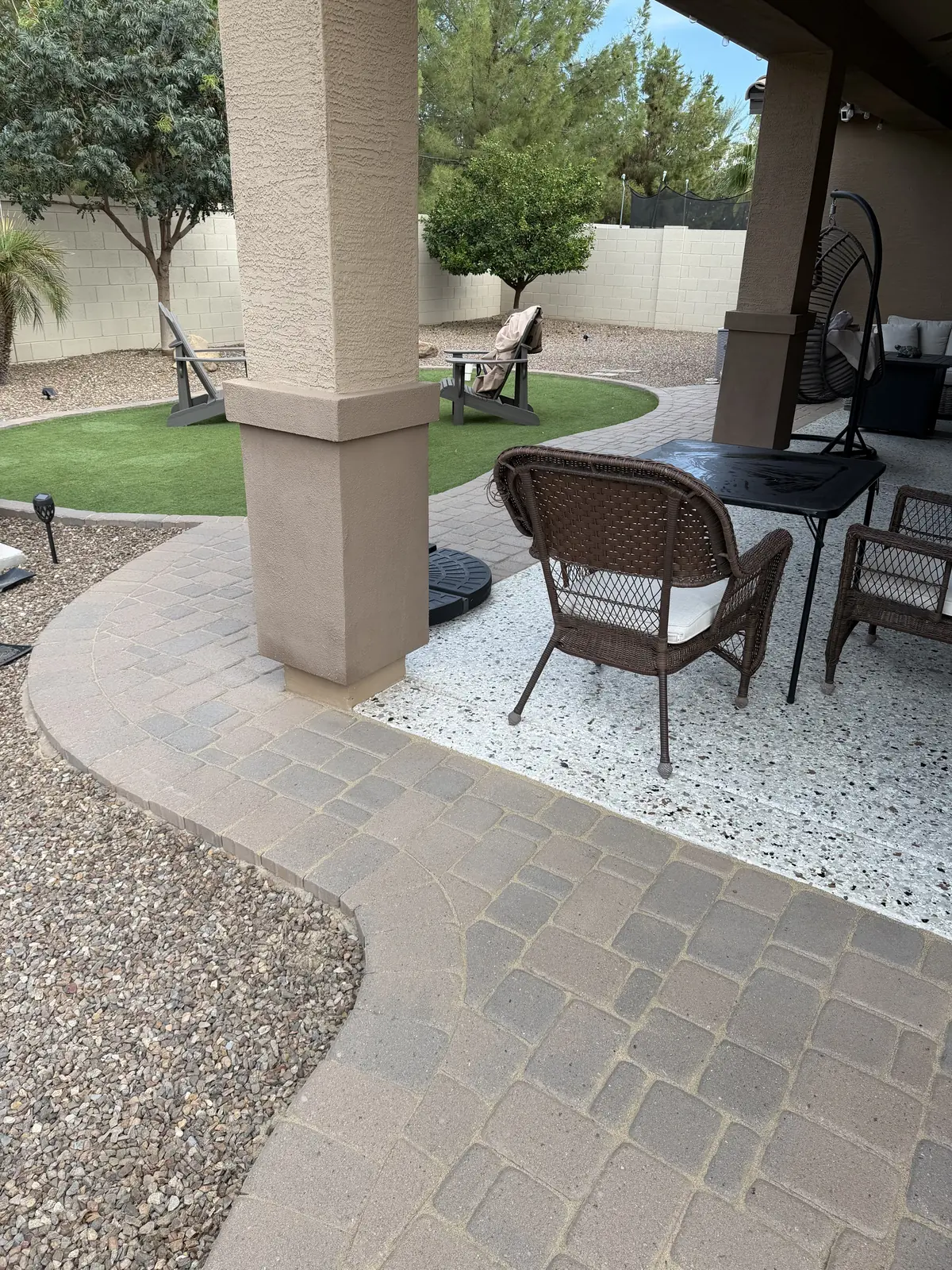 Backyard patio seating and a table on clean pavers next to turf and a block wall